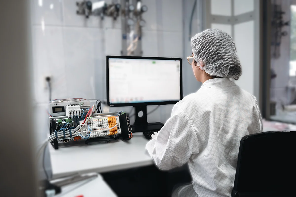 Laboratory technician in protective clothing operating analytical equipment in a cleanroom.