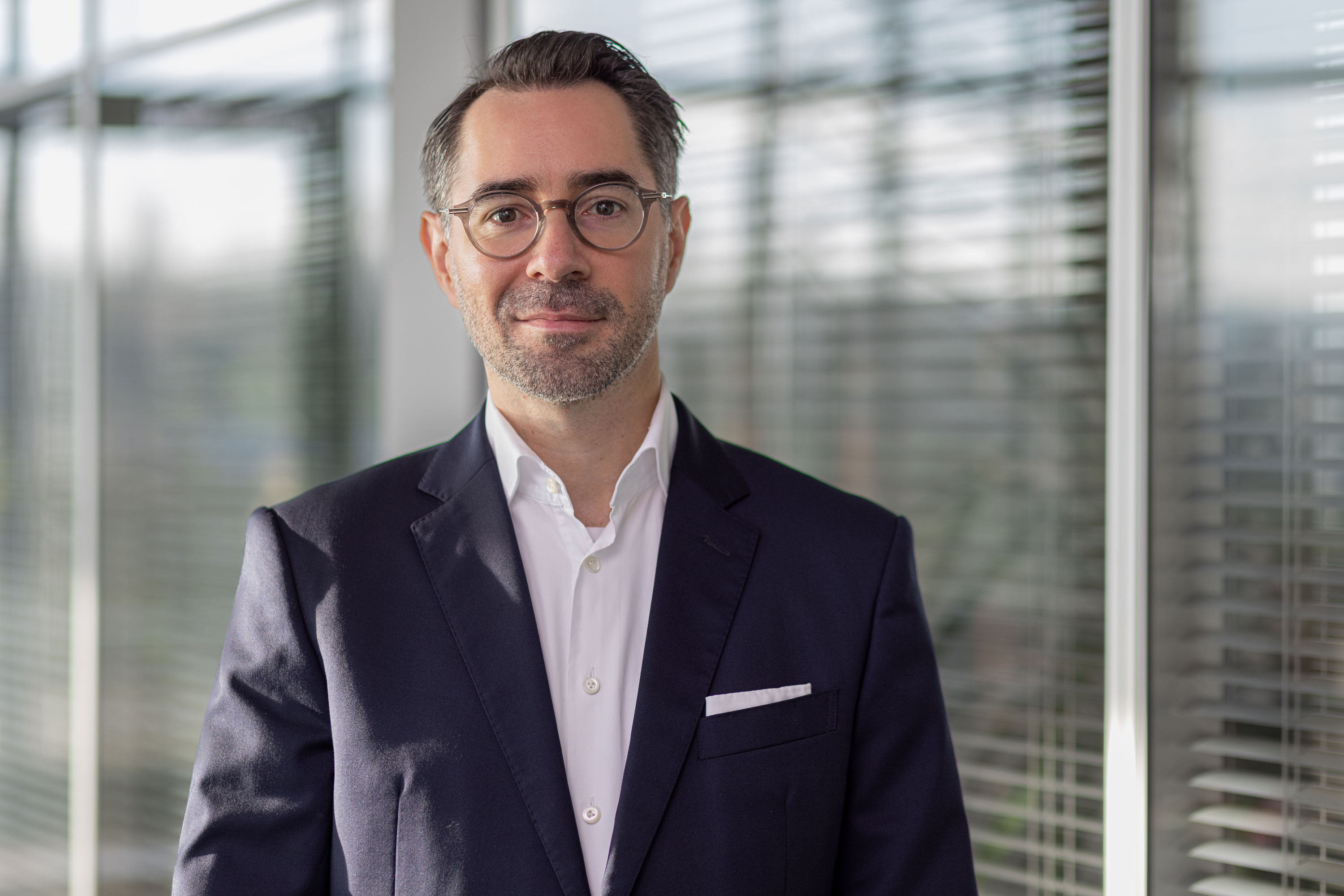 A professional man in a dark suit and white shirt stands in an office, representing the expertise behind PVA TePla semiconductor equipment solutions.